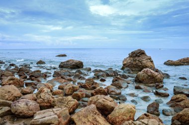 Kayalar arka planda açık bir gökyüzü ile denizi gümbürdetir..