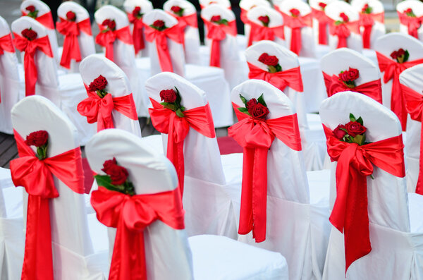 Wedding chairs decorated in white, ribbons and red rose.