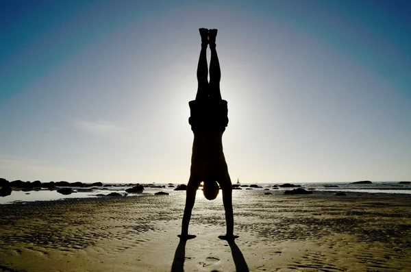 Мужчина делает йогу вверх ногами на пляже — стоковое фото