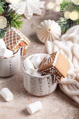 Bej arka planda mini zencefilli ev ile süslenmiş beyaz bardakta sıcak kakao. Noel konsepti.