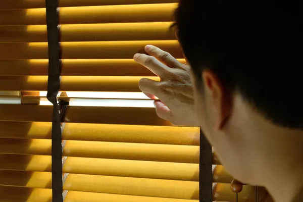 Um homem está a olhar através das cortinas — Fotografia de Stock