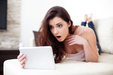 Surprised woman with tablet on couch clipart