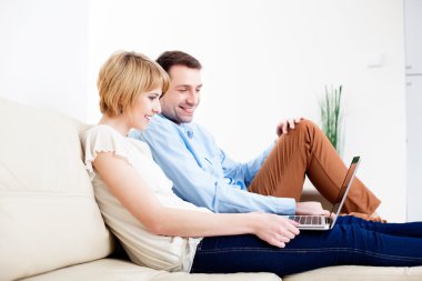 dizüstü bilgisayar kullanan kanepede oturan genç bir çift