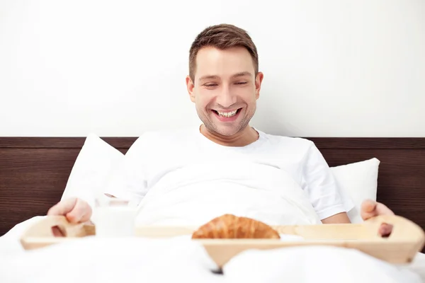 Happy single man eating breakfast in bed — Stock Photo, Image