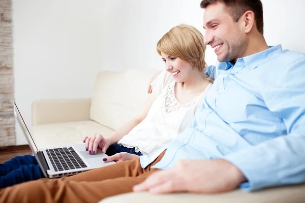 坐在沙发上使用的便携式计算机上的年轻夫妇 — 图库照片