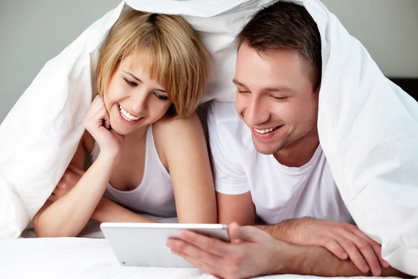 Happy couple lying in bed with digital tablet — Stock Photo, Image