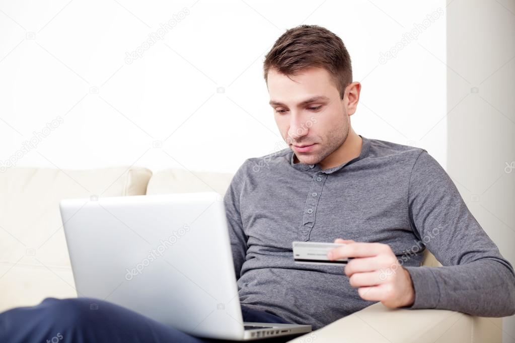 Handsome man holding credit card and using his laptop