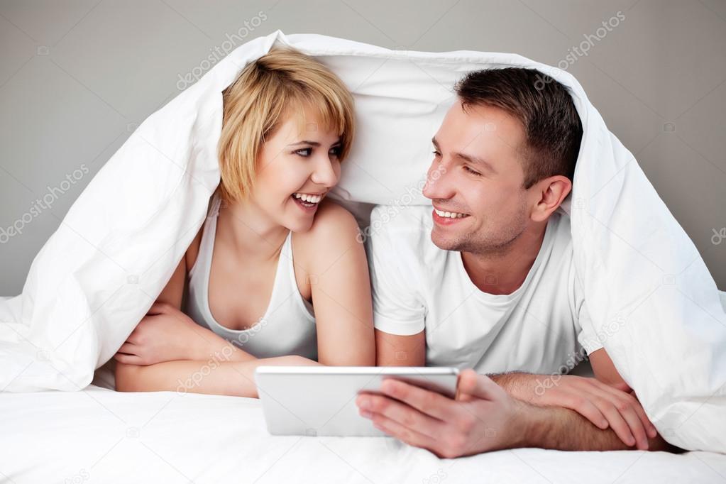 Happy couple lying in bed with digital tablet