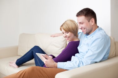 mutlu genç bir çift dijital tablet kullanarak kanepede oturan