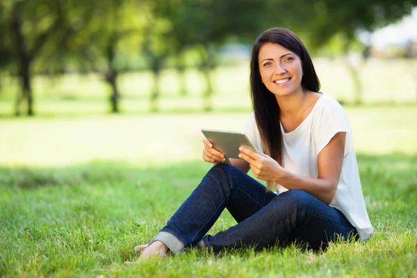 Hermosa mujer joven con tableta digital sentado en la hierba en pa —  Fotos de Stock