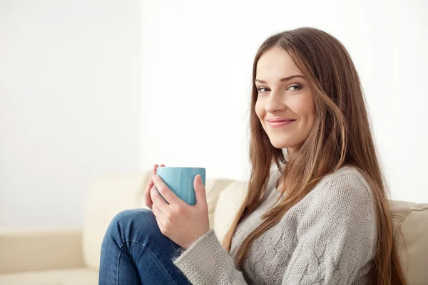 Mujer joven feliz con taza de té sentado en el sofá — Foto de Stock