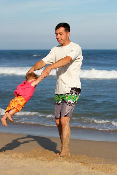 Pappa med ett barn leker på stranden vid havet — Stockfoto