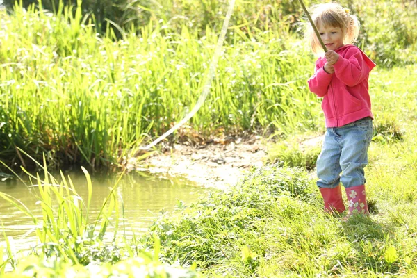 Mooi meisje buiten in de buurt van een meertje in rubberen laarzen — Stockfoto