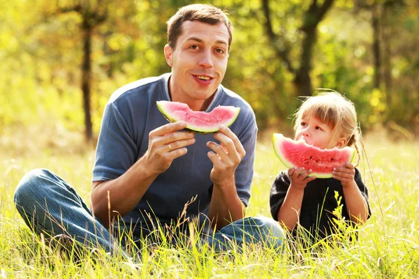 Beautiful little girl with dad in nature eating watermelon