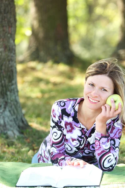 Young woman eating an apple and reading a book the Bible — Stock Photo, Image