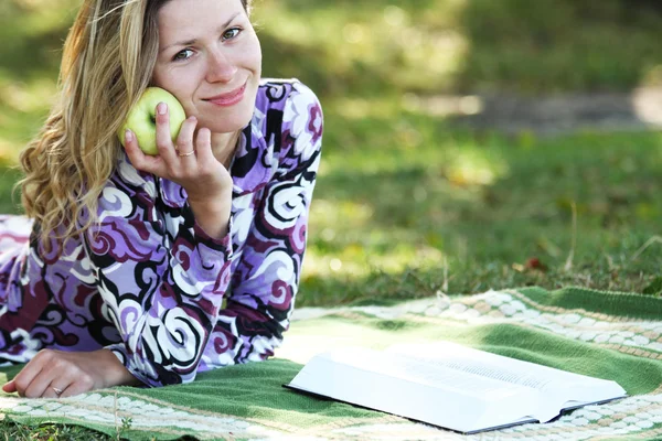 Молодая женщина ест яблоко и читает книгу Библию — стоковое фото