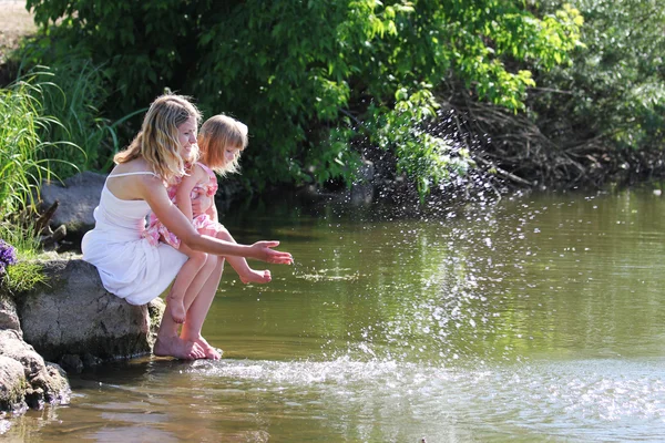 Mother and her little daughter squirting water at the lake — Stock Photo, Image