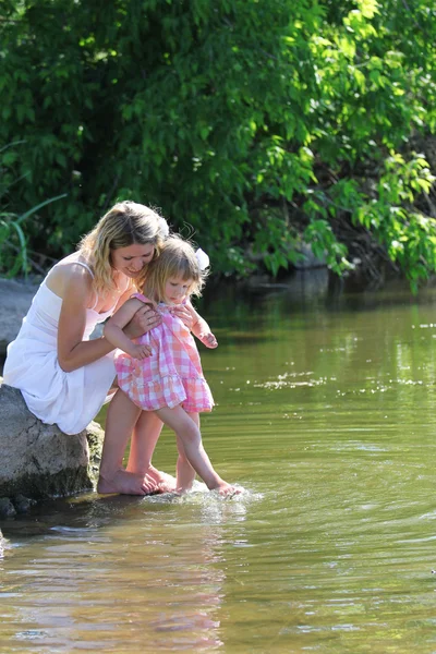 Mother and her little daughter squirt water at the lake — Stock Photo, Image