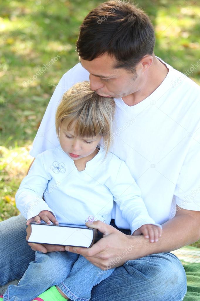 father with a young daughter read the Bible in nature