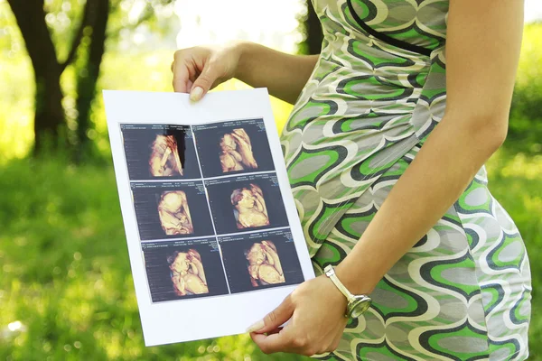 Pregnant girl on nature with ultrasound photos — Stock Photo, Image