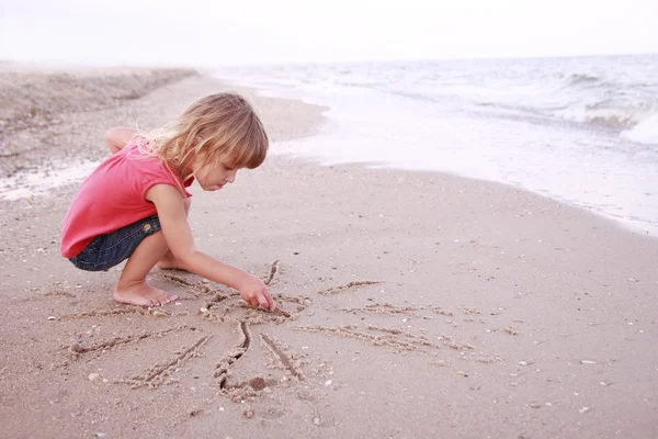 Chica dibuja un sol en la arena en la playa —  Fotos de Stock