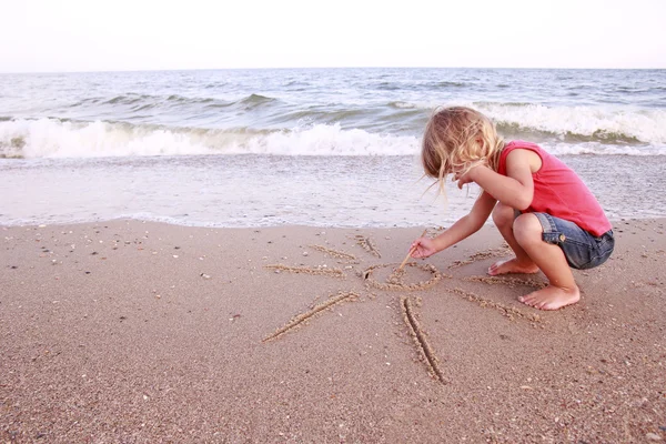 Fille dessine un soleil dans le sable sur la plage — Photo