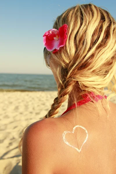 Corazón de la crema en la espalda femenina en la playa — Foto de Stock