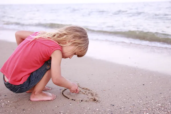Klein meisje trekt een zon in het zand op het strand — Stockfoto