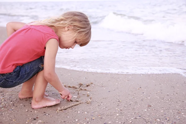 Little girl draws a sun in the sand — Stock Photo, Image