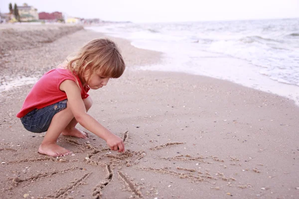 Petite fille dessine dans le sable sur la plage — Photo