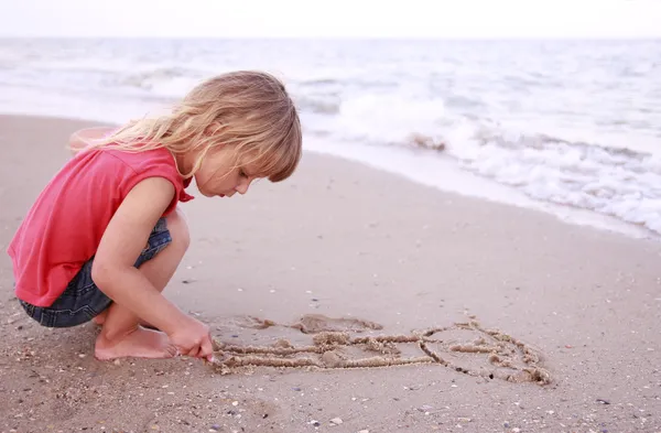 Klein meisje tekent in het zand op het strand — Stockfoto