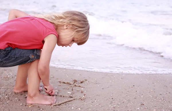 Klein meisje trekt een zon in het zand op het strand — Stockfoto