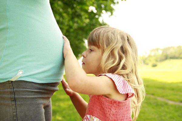 Klein meisje in de buurt van de buik van zijn zwangere moeder over aard — Stockfoto