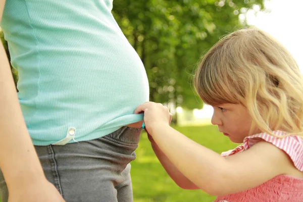 Klein meisje in de buurt van de buik van zijn zwangere moeder over aard — Stockfoto