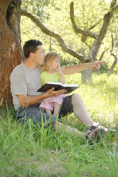 Padre joven con su pequeña hija lee la Biblia — Foto de Stock