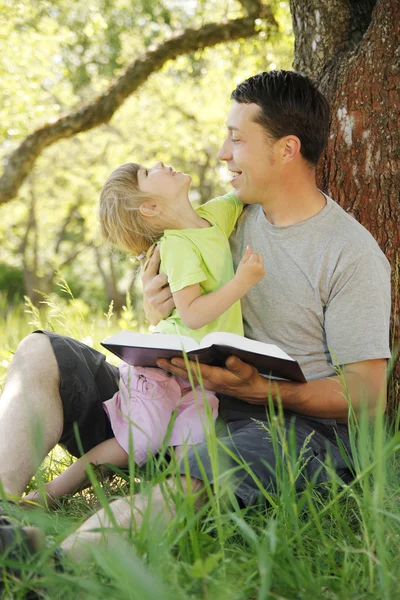 Padre joven con su pequeña hija lee la Biblia —  Fotos de Stock