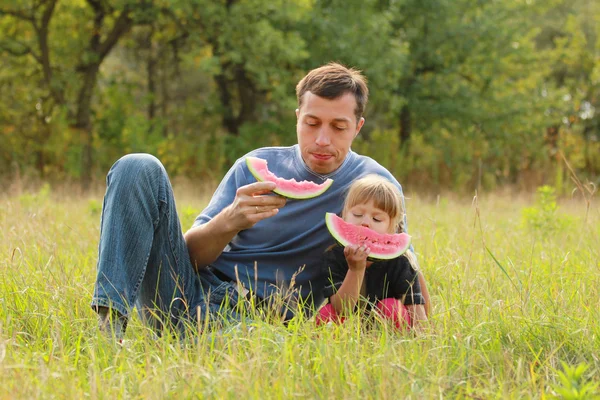 父と若い娘は自然の中でスイカを食べる — ストック写真