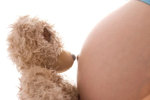 Беременная женщина с плюшевым мишкой на белом фоне — стоковое фото