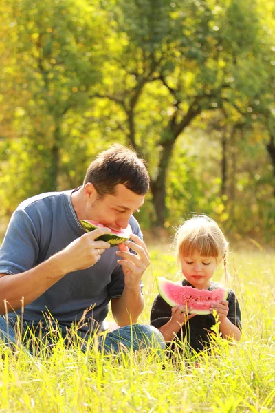 Hermosa niña con su padre come sandía en la naturaleza — Foto de Stock