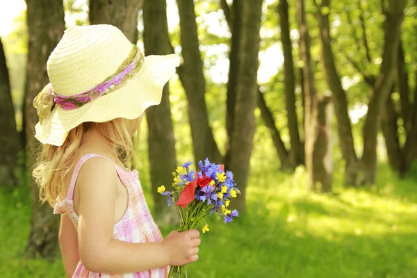 Vacker liten flicka med en bukett blommor i naturen — Stockfoto