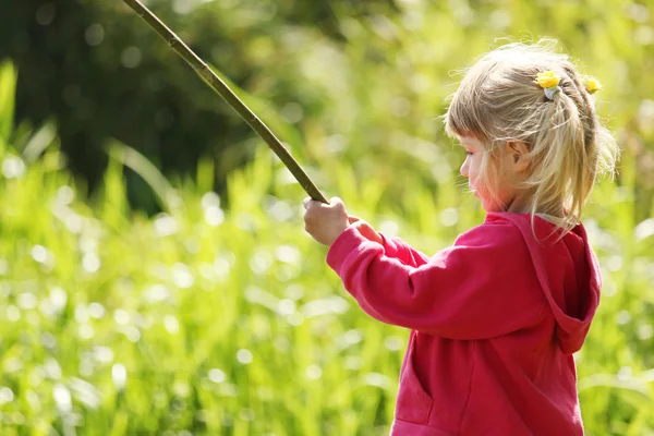 Красивая маленькая девочка на природе, играющая с палкой — стоковое фото