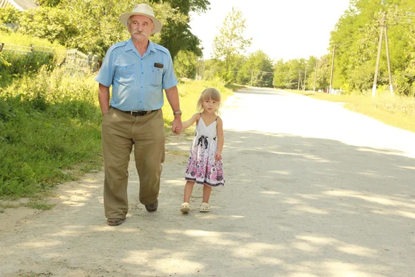 Дедушка с внучкой идут по дороге — стоковое фото