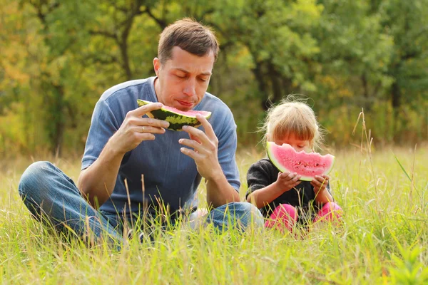 Pai com uma pequena filha comer melancia na grama — Fotografia de Stock