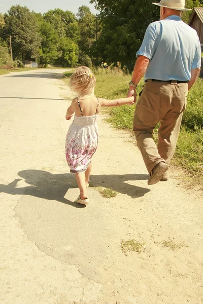 Дедушка с внучкой идут по дороге — стоковое фото