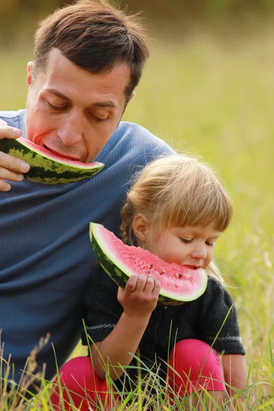 Батько з маленькою дочкою їсть кавун на траві — стокове фото