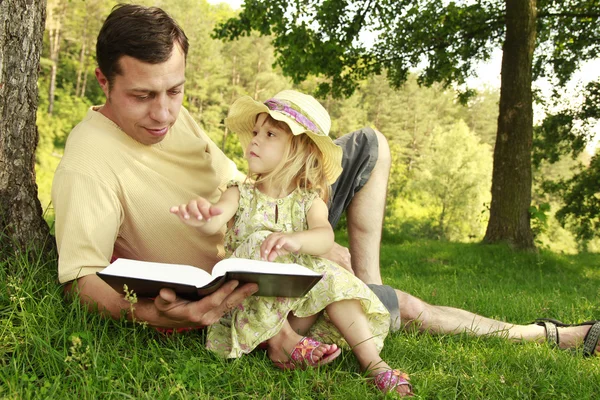 Padre joven con su pequeña hija lee la Biblia — Foto de Stock