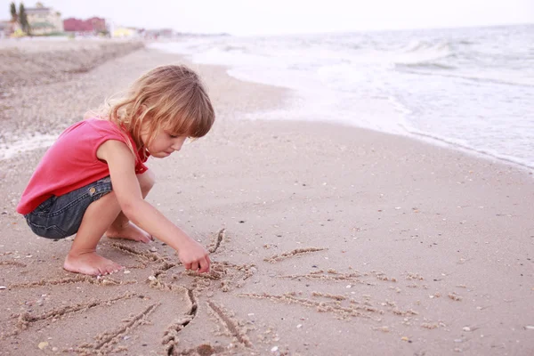 Klein meisje trekt een zon in het zand aan de kust — Stockfoto