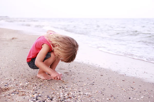 Klein meisje trekt een zon in het zand aan de kust — Stockfoto