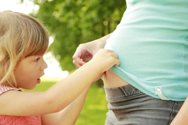 Pequena filha com uma barriga de uma mãe grávida natureza — Fotografia de Stock