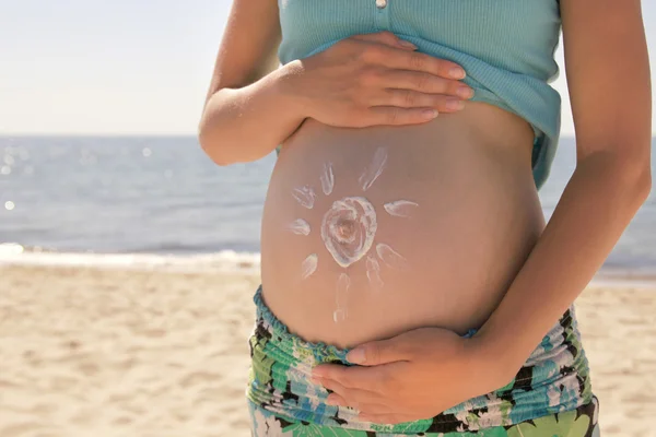 Güneş hamile bir kadının karnında plaj üzerinde krem — Stok fotoğraf